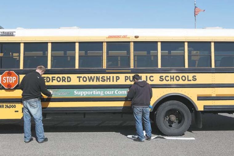 Robert Fandel (left) and Leonardo Valencia (right), sign installers, apply an advertising sign to the side of a Medford Township school bus. Fifty four school buses had the signs applied. March 5, 2013. ( MICHAEL S. WIRTZ / Staff Photographer ).