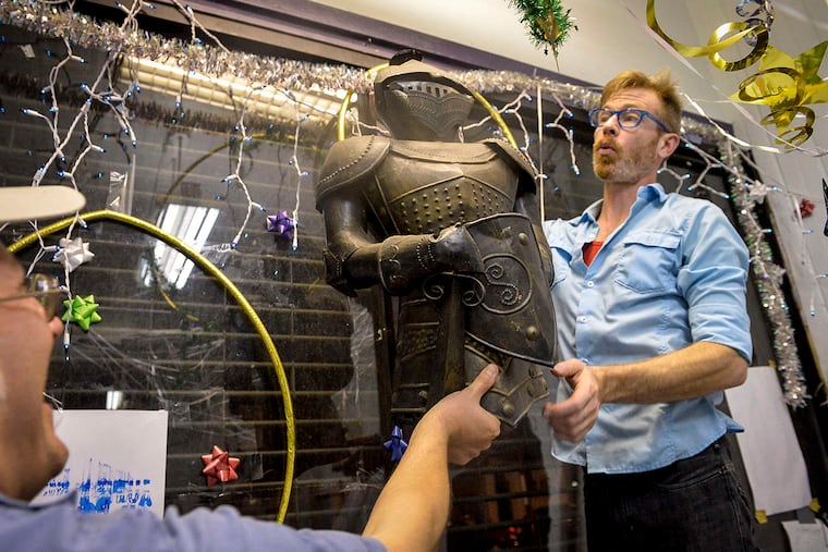 Matt Stevenson, left, and Daniel Baker try to hang a suit of armor in the Eris Temple Artspace in West Philadelphia.