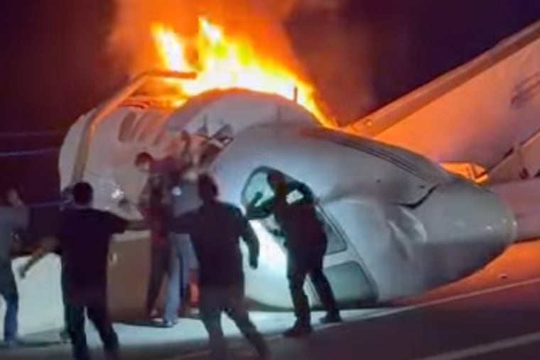 A passenger jumps out of a plane after it crashed on a highway as other people help Tuesday in Laredo, Texas.