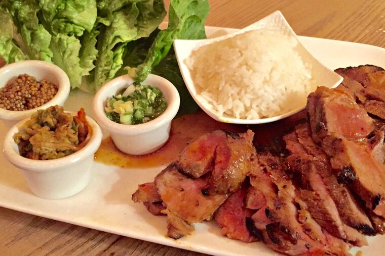 A pork bossam with sides of lettuce, rice, scallions, kimchi, and mustard seeds.