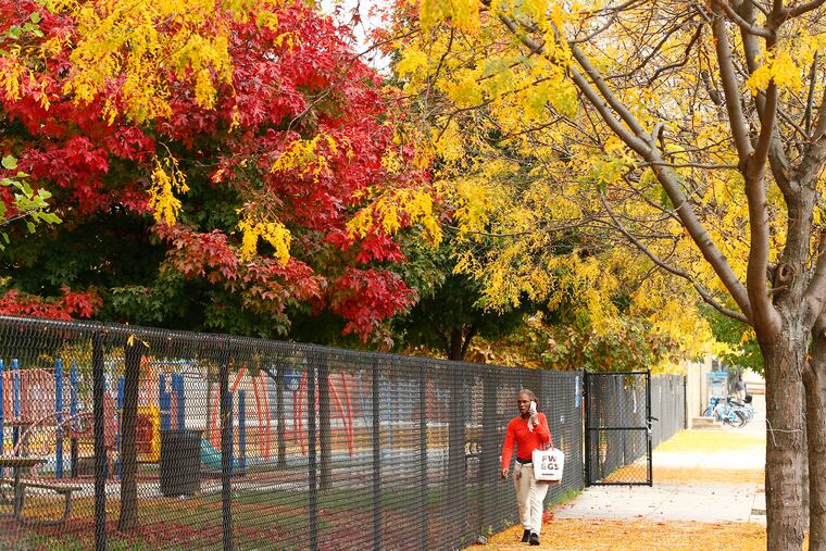 A pedestrian walks under trees changing colors to a fall foliage at the Hank Gathers Recreation Center in North Philadelphia late last October.