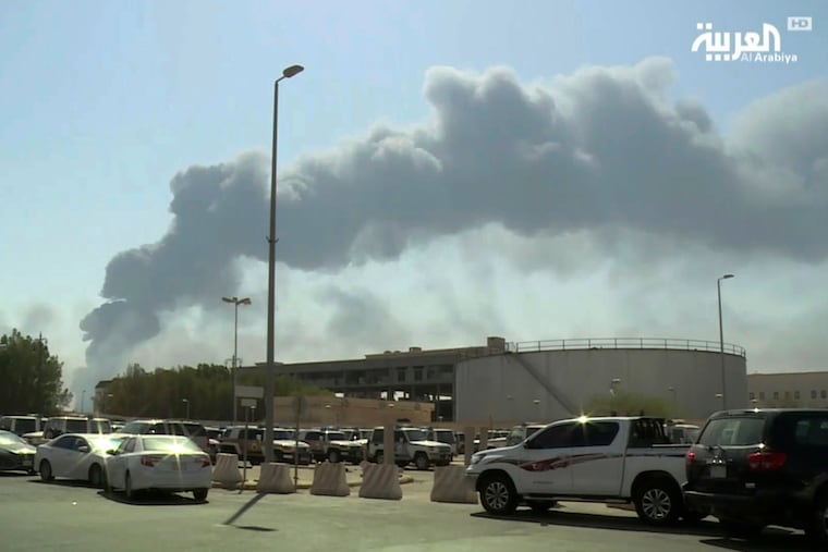 In this photo made from a video broadcast on the Saudi-owned Al-Arabiya news channel, a man walks through a parking lot as the smoke from a fire at the Abqaiq oil processing facility can be seen behind him in Buqyaq, Saudi Arabia, Sept. 14, 2019. The Saturday morning attacks, claimed as drone attacks by Yemen’s rebel Houthis, against the state-owned company led to a suspension of around 5% of the world’s daily crude oil production.