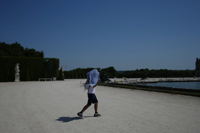A man shields himself from the sun with a scarf as he walks in the garden of the Palace of Versailles, outside Paris, during a heat wave with temperatures soaring above 40 degrees Celsius (104 Fahrenheit), Monday, June 22, 2026.