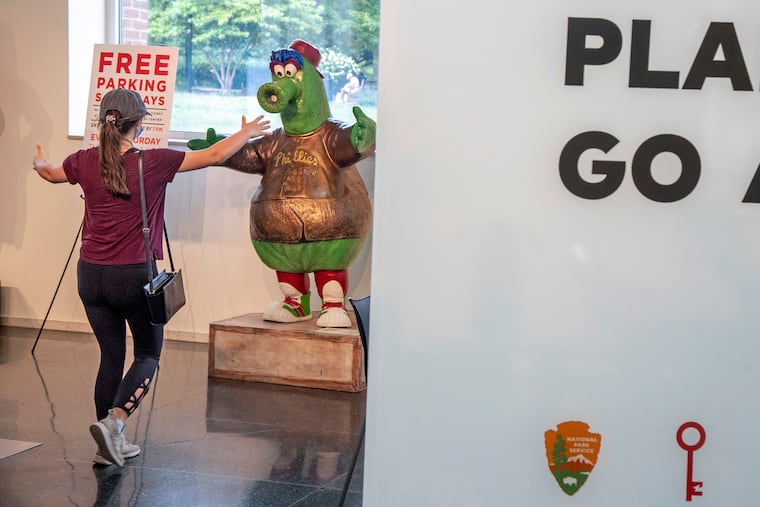 June 21, 2021: A tourist approaches the Phillie Phanatic statue at the Independence Visitor Center. The team mascot was one of a phlock of 20 Phanatics that were decorated by different local artists and spread around the city in 2010 as part of a tourism campaign. All the other fiberglass statues were auctioned off for charity at the end of the summer.