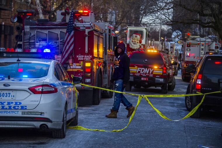 A resident walks as police and firefighters work at the scene near the building where twelve people died in a fire a day earlier, on Friday, Dec. 29, 2017, in the Bronx borough of New York.