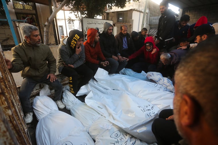 Palestinians sit by the bodies of the Dhair family, killed in the Israeli bombardment of the Gaza Strip, during their funeral in Rafah on Friday, Dec. 22, 2023.