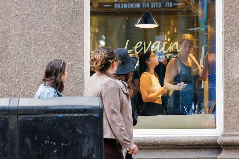 Elaine Dehart and Tara Jacoby (right) working on mural inside the soon to open Levain Bakery as pedestrians peer in the window along Walnut Street.