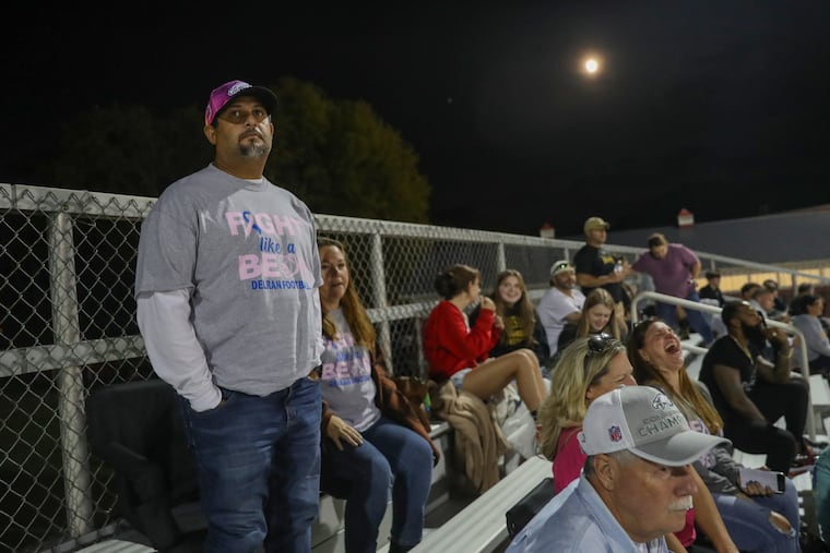 Juan Namnun sits next to his wife, Lena Namnun, as they watch two of their sons play in a football game at Rancocas Valley Regional High School in Mt. Holly on Friday. Namnun, a former baseball player turned longtime coach and educator at Frankford High School, is battling breast cancer.