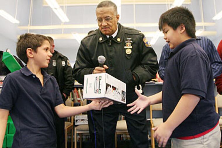Juniata Park Academy student Janny Navarreto gives a toy truck to schoolmate William Bui as Deputy Commissioner Stephen
Johnson and Police Officer Eddie Lopez Sr. look on. The gift-giving was part of the Philadelphia Police Department's 12th annual "Spirit of Giving" Christmas program.