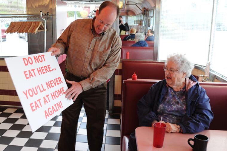 Ken Weinstein, owner of the Trolley Car Diner, shows a patron, Clara Aldrich, 72, of Wyndmoor, one of the signs he is placing in front of the diner April 23, 2014, to counter signs by the IBEW Local 98 union urging customers not to eat at the diner. The union is staging the action because Weinstein owns a development company that uses non-union labor. (CLEM MURRAY/Staff Photographer)