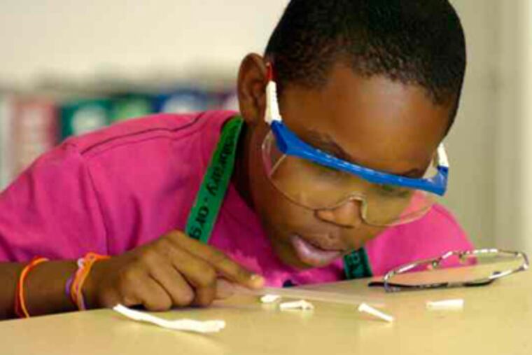 Cameron Gills tries to pick up a small piece of paper with a statically charged straw in the GlaxoSmithKline program, which helps students retain lessons learned during the school year. (Ron Tarver / Staff Photographer)