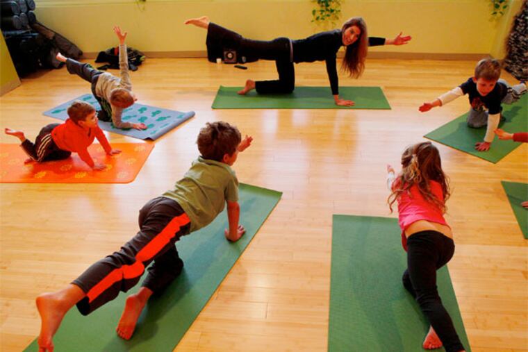 Instructor Lauren Robertson guides students (clockwise) Ryan Schaeffer,6, Gabriel Schrieber, 5, Alyiah Brownstein, 5, Zach Brownstein, 8, Reid Reichman, 4, and Aiden Reichaman, 7, into a pose during a Kids class at the Yoga Garden in Narberth. ( MICHAEL S. WIRTZ / STAFF PHOTOGRAPHER ).