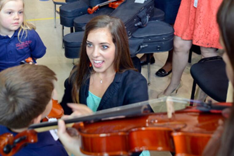 Music teacher Ashley Martelli (cq-24 yrs) helps incoming students at the Philadelphia Charter School for the Arts and Sciences at H.R. Edmunds hold some of the 800 just-delivered string instruments at the brand-new Renaissance school August 23, 2012, before a press conference for the non-profit Philadelphia School Partnership to announce over $50 million in funding has been committed towards the $100 Great Schools Fund. Martelli teaches at the Philadelphia Performing Arts Charter School, in South Phila. which is managed by String Theory Schools, which will also manage the School for the Arts and Sciences at H.R. Edmunds. In background are teachers from both Performing Arts Charter and Charter School for the Arts and Sciences, readying some instruments. ( TOM GRALISH / Staff Photographer )