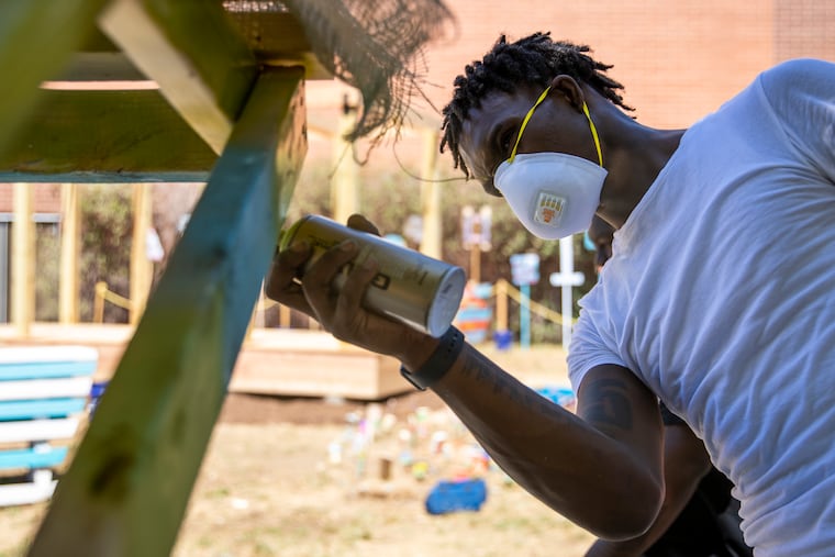 Naasir Davis, 19, of West Philadelphia, spray paints one of the benches in the new courtyard made in the Design to Thrive program with graduate students from the Weitzman School of Design and teens at West Philadelphia High School on Aug. 3, 2022.