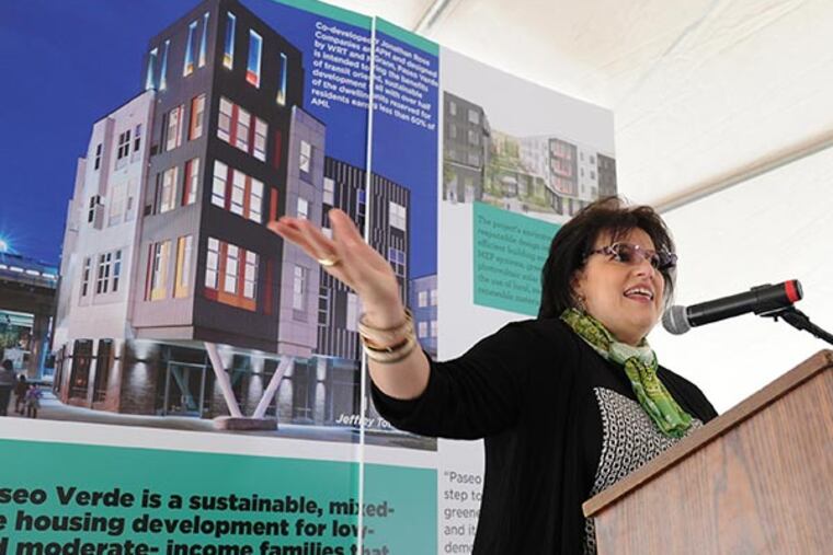 Nilda Ruiz, president of Asociación Puertorriqueños en Marcha, speaks at a ribbon-cutting ceremony for Paseo Verde, a complex of 120 affordable and market-rate apartments at Ninth and Berks Streets in North Philadelphia, Dec. 3, 2013. The photo behind Ruiz shows the complex. (CLEM MURRAY / Staff Photographer)