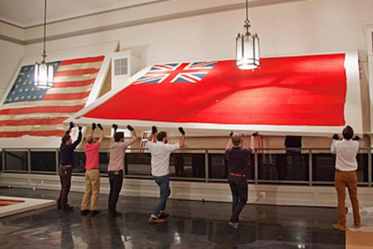 Art handlers hoist a rare English naval red ensign into place in Freeman’s first-floor gallery. A collection of rare naval flags will be offered for sale at the auction house Monday. ELIZABETH FIELD / Freeman’s