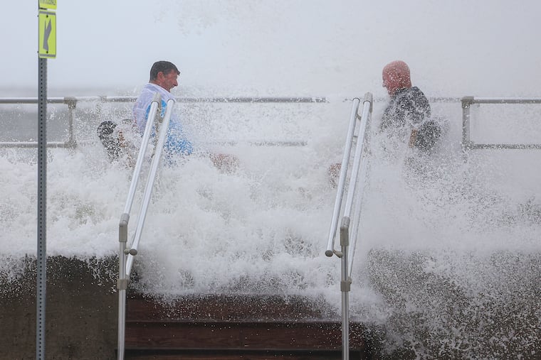 Friends Dennis Donnelly (left) and Jack Sharkey (right) of Northeast Philadelphia, are soaked as the surf crashes over the North Wildwood sea wall in North Wildwood, N.J. on Sunday, Oct. 12, 2025. Donnelly said they were in the area to retrieve his jet ski to prevent it from getting damaged by the storm.