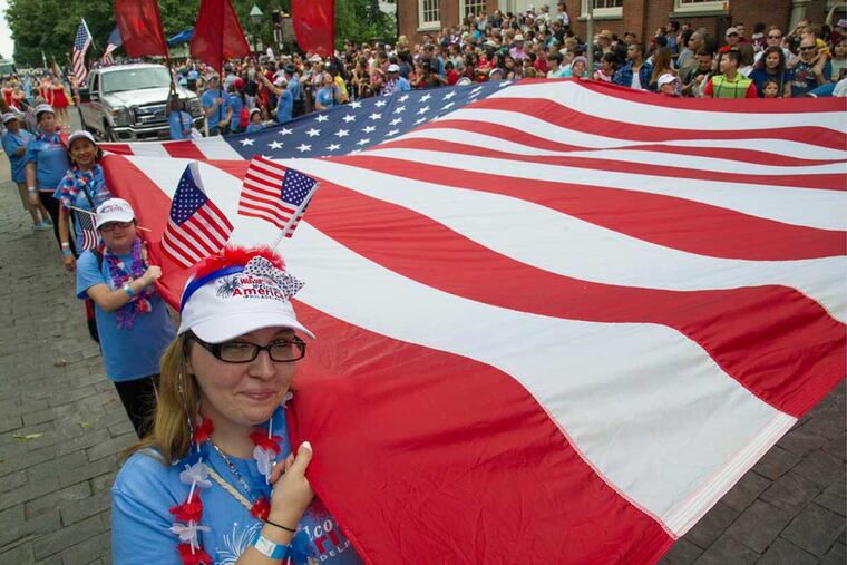 Shelby Frank, 23, of Phillipsburg, N.J., wears a pair of flags as she helps carry the oversized flag to start Philadelphia's Fourth of July parade along Chestnut Street in 2015.