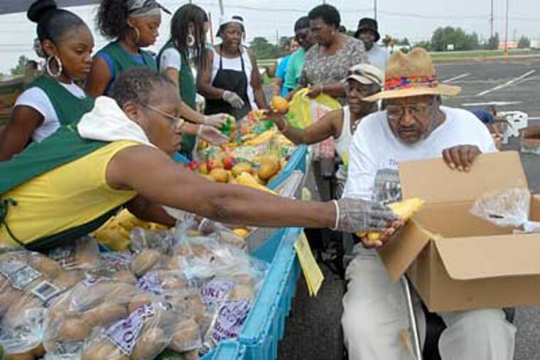 Outside the Grand Marketplace, volunteer Dottie Tutt of Philadelphia, gives Prince Nance of Willingboro a hand with the food he's picking up. (April Saul/Inquirer)