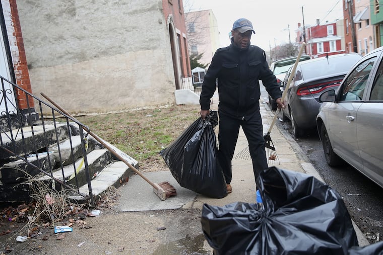 Ernest Gardner carries a bag of trash after raking it off of his block on North 19th Street in North Central Philadelphia in February.