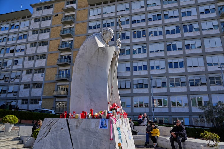 People sit by the statue of Pope John Paul II outside the Agostino Gemelli Polyclinic, where Pope Francis is hospitalized in Rome on Tuesday.