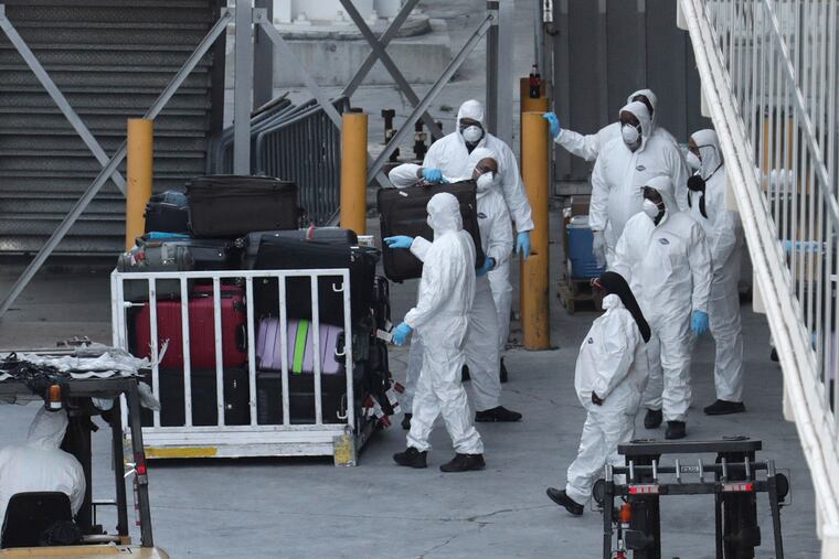 Workers in protective gear unload luggage from Carnival's Holland America cruise ship Zaandam as it is docked at Port Everglades.