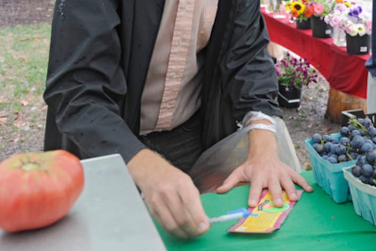 Bench Ansfield pays for his tomato at the farmers' market at Clark Park in West Philadelphia, using Philly Bucks. (Clem Murray / Staff Photographer)