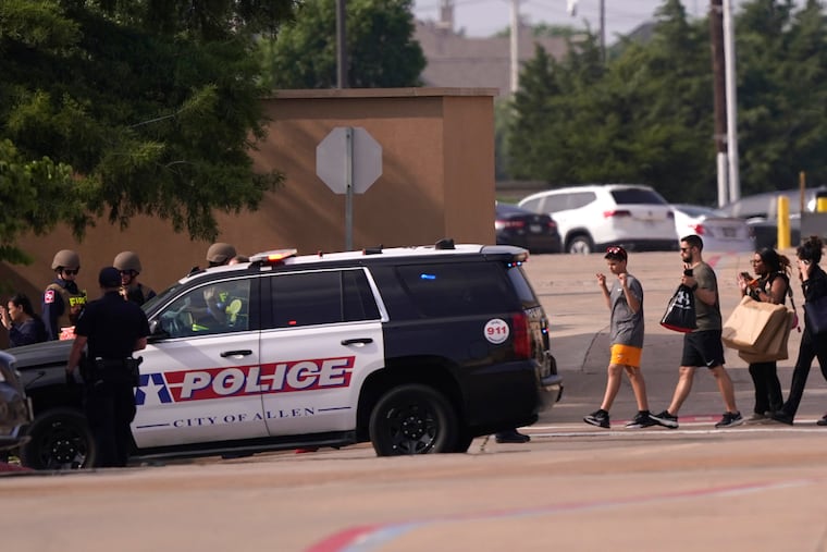 People raise their hands as they leave a shopping center after a shooting Saturday in Allen, Texas.