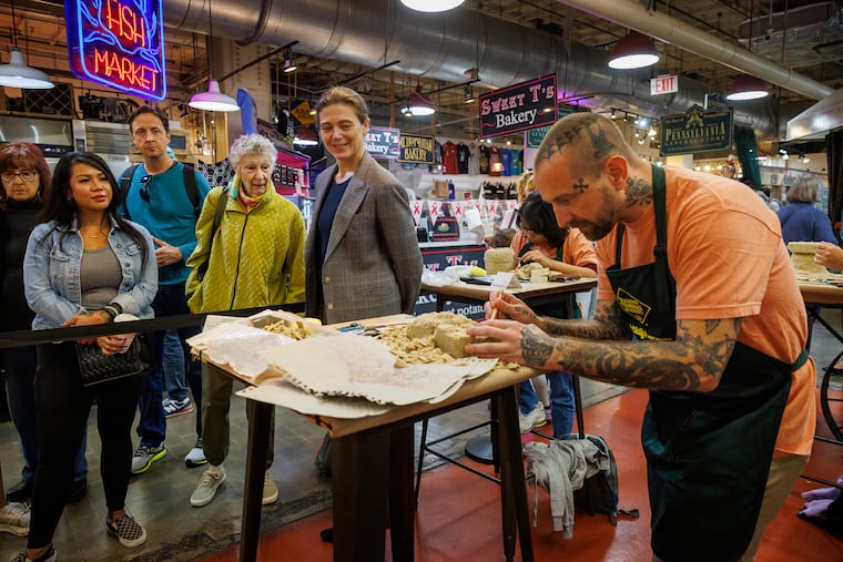 Philadelphia Art Museum director and CEO Sasha Suda watches Patrick Moser carving his "Mush Push" sculpture out of scrapple during the second annual Scrapple Sculpting Contest at Reading Terminal Market Friday.