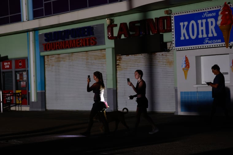 Dog walkers use the flashlights and lights on their cell phones along the Wildwood Boardwalk after the power went out in Wildwood, New Jersey on Friday, July 7, 2023.