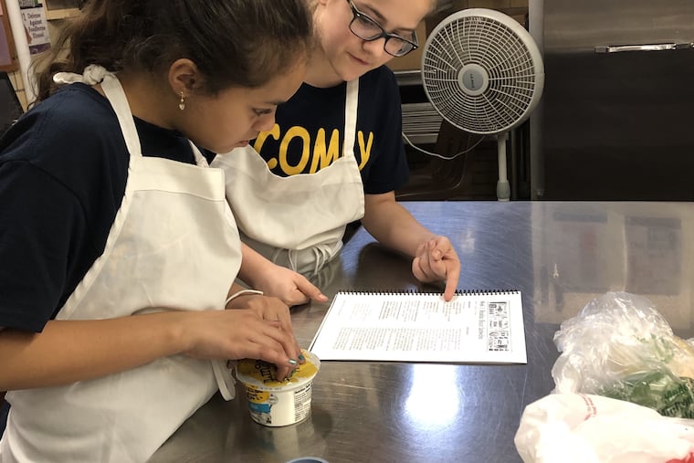 Cheyana Rivas and Erica Gogan read the recipe for Breakfast Biscuit Sandwiches during week 1 of the Spring 2019 My Daughter's Kitchen cooking program at Comly School.