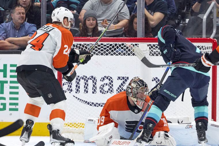 Seattle Kraken right wing Jordan Eberle, right, digs for the puck on a shot blocked by Flyers goaltender Carter Hart, with Flyers defenseman Nick Seeler looking on.