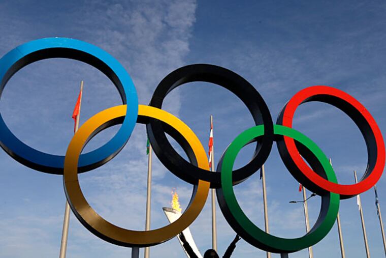 A spectator poses for a photo under the Olympic Rings at the 2014 Winter Olympics, Wednesday, Feb. 12, 2014, in Sochi, Russia. The Winter Olympics are in full swing, but warm temperatures in the Black Sea resort town of Sochi made heavy coats and scarves unnecessary on Wednesday. (Mark Baker/AP)