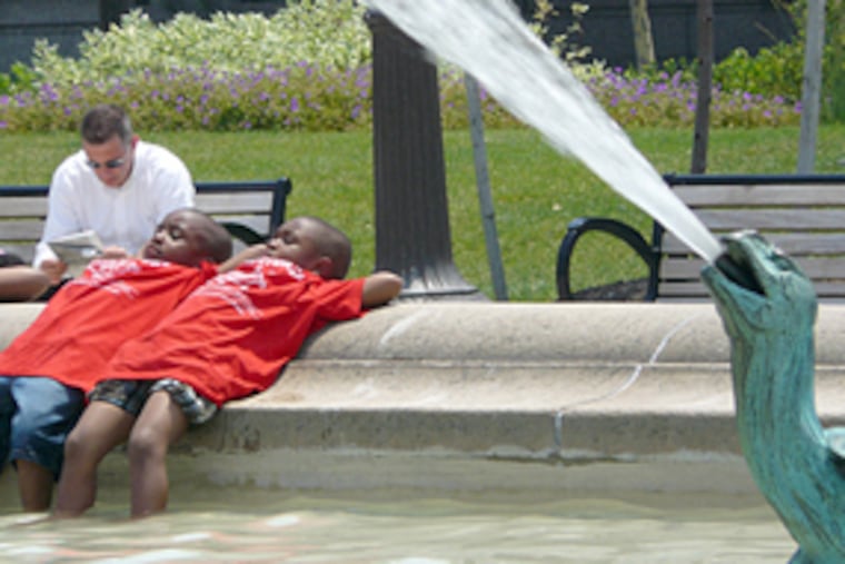 Mugahib Jamaddlin, left, and Nashyne Dawkins lounge on the side of Swann Fountain on the Benjamin Franklin Parkway in Center City. The children, from the R.W. Brown Community Center in North Philadelphia, were on a day trip to the Academy of Natural Sciences and detoured across the Parkway to cool off at the fountain.