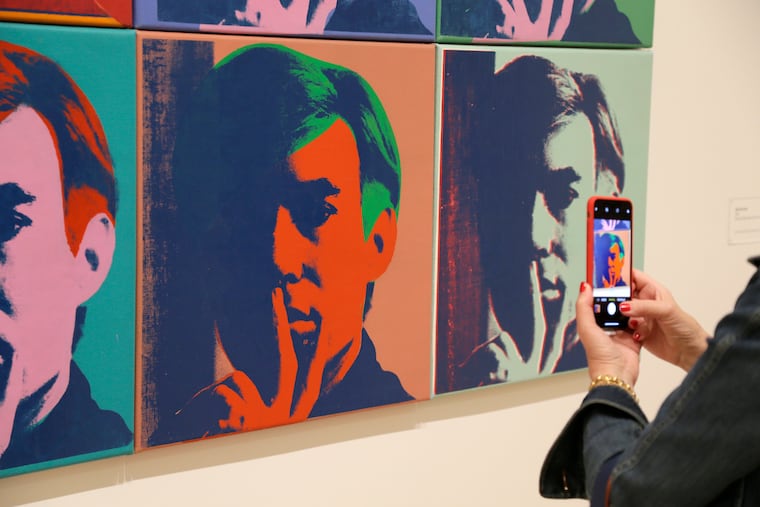 In this photo taken Wednesday, May 15, 2019, a woman records one of a series of self portraits at the exhibition, "Andy Warhol _ From A to B and Back Again", in San Francisco. A retrospective of Andy Warhol's work on display at the San Francisco Museum of Modern Art captures his use of artwork to give his subjects personas the way people do now using social media. (AP Photo/Eric Risberg)