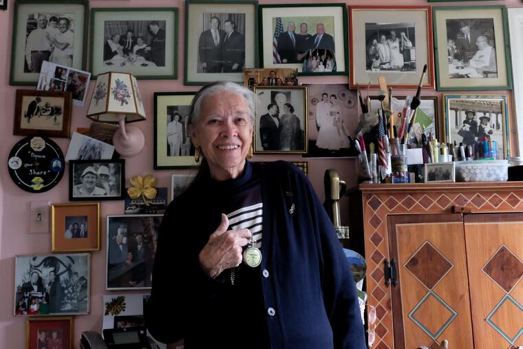In the kitchen of her Haverford hone, Constance Bookbinder holds her father's pocket watch that connects her to the 1937 Hindenburg zeppelin disaster. On the wall behind her are framed photos of celebrities from now-closed Bookbinder's 15th Street restaurant in Philadelphia.