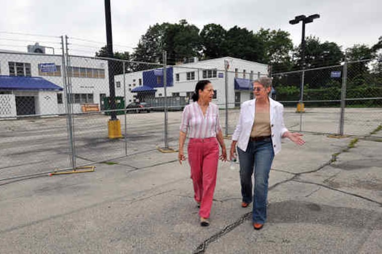 Meg Greenfield (left), vice president of the East Falls Community Council, and Carolyn Sutton, head of the East Falls Development Corp., object to housing a school in the buildings beyond.