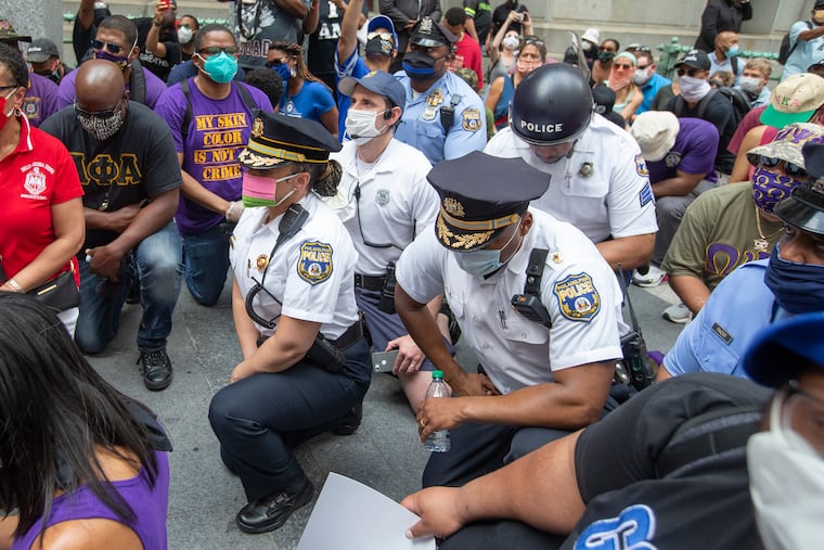 Philadelphia Police Commissioner Danielle Outlaw (left) and police officers take a knee as George Floyd is remembered. Outlaw marched with the Black Greek fraternities.