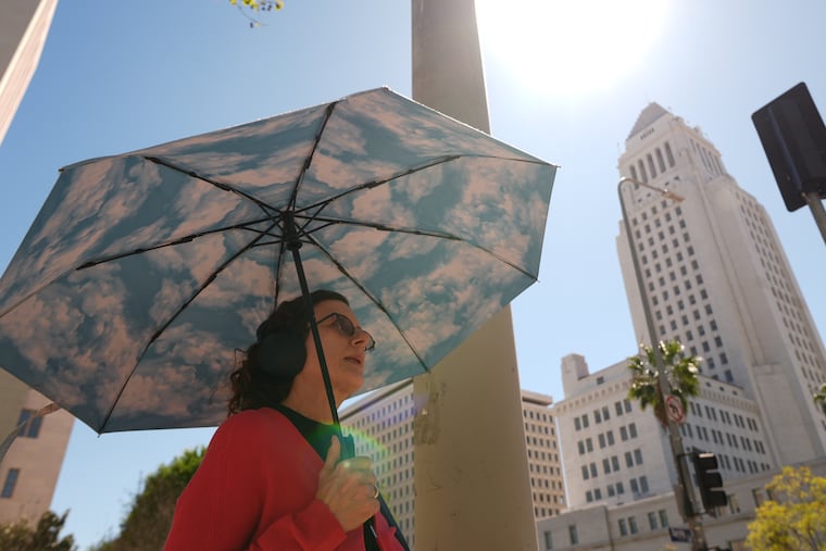 A pedestrian holds a cloud themed umbrella under a sunny day next to Los Angeles City Hall in Los Angeles Thursday, March. 12, 2026.