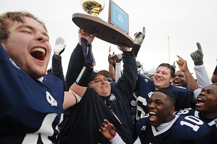West Catholic coach Brian Fluck hoists the PIAA AA State Championship trophy while surrounded by his team. (Bob Williams/For the Inquirer)
