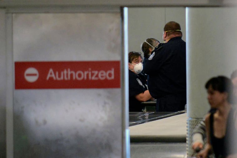 Masked customs officers look on during a screening area for international passengers from United flight 998 from Brussels at Newark airport in Newark, N.J., Saturday, Oct. 4, 2014. New Jersey health officials say Ebola has been ruled out as the cause of illness for a man who became sick on a flight from Brussels to the United States (AP Photo/Northjersey.com, Viorel Florescu)