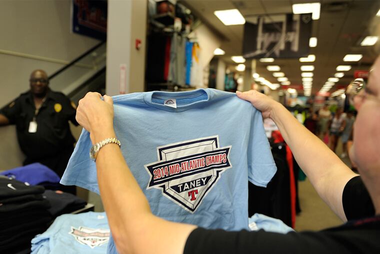Security guard Anthony Townsend watches as customer Janet Brindley of Havertown sizes Taney t-shirt for purchase at Modell's on Chestnut Street August 19, 2014 as demand is through the roof for Taney Little League gear.