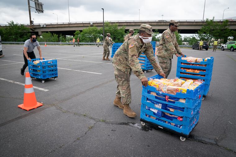 National Guard Specialist Dimir Brunson, front left, and others cart food through a parking lot next to Philadelphia's sports stadiums for Philabundance's drive-through food distribution on Friday.