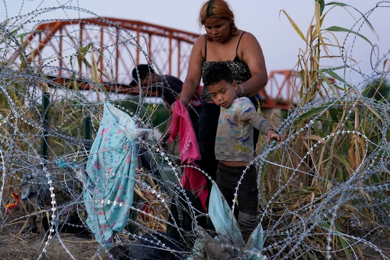Migrants climb over concertina wire after they crossed the Rio Grande and entered the U.S. from Mexico, Saturday, Sept. 23, 2023, in Eagle Pass, Tex.