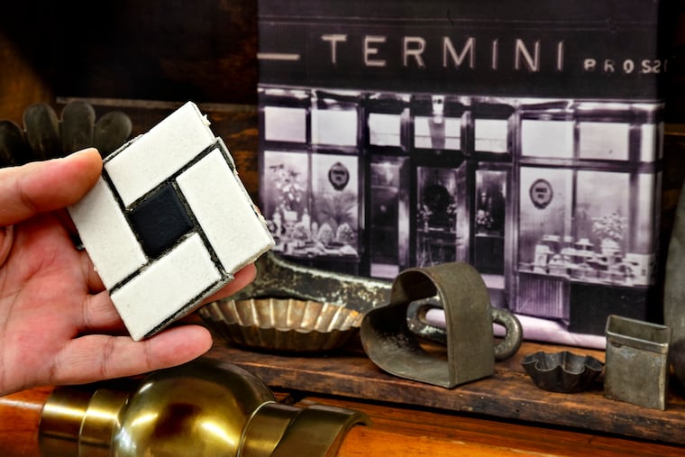 Joey Termini holds a section of the original black-and-white porcelain pinwheeled-tiled floor, near a display of artifacts at Termini Brothers bakery on Monday, July 31, 2023. His grandfather, founder Joseph Termini and his brother, Gaetano, handpicked the design in 1938. The flooring was recently replaced, and Joey and his brother Vinny Termini plan to offer pieces of the old tiles to customers.