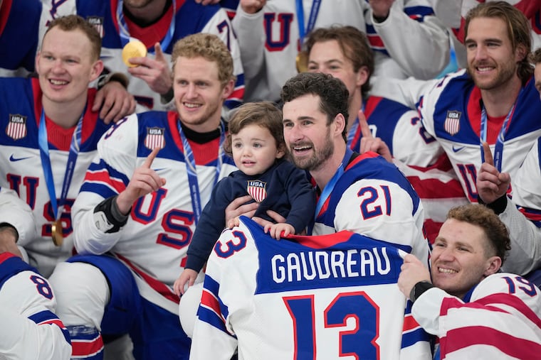 The U.S. team's Dylan Larkin (21) holds Johnny Gaudreau Jr., the son of the late NHL star, as the team celebrates its gold medal victory against Canada at the Olympics.