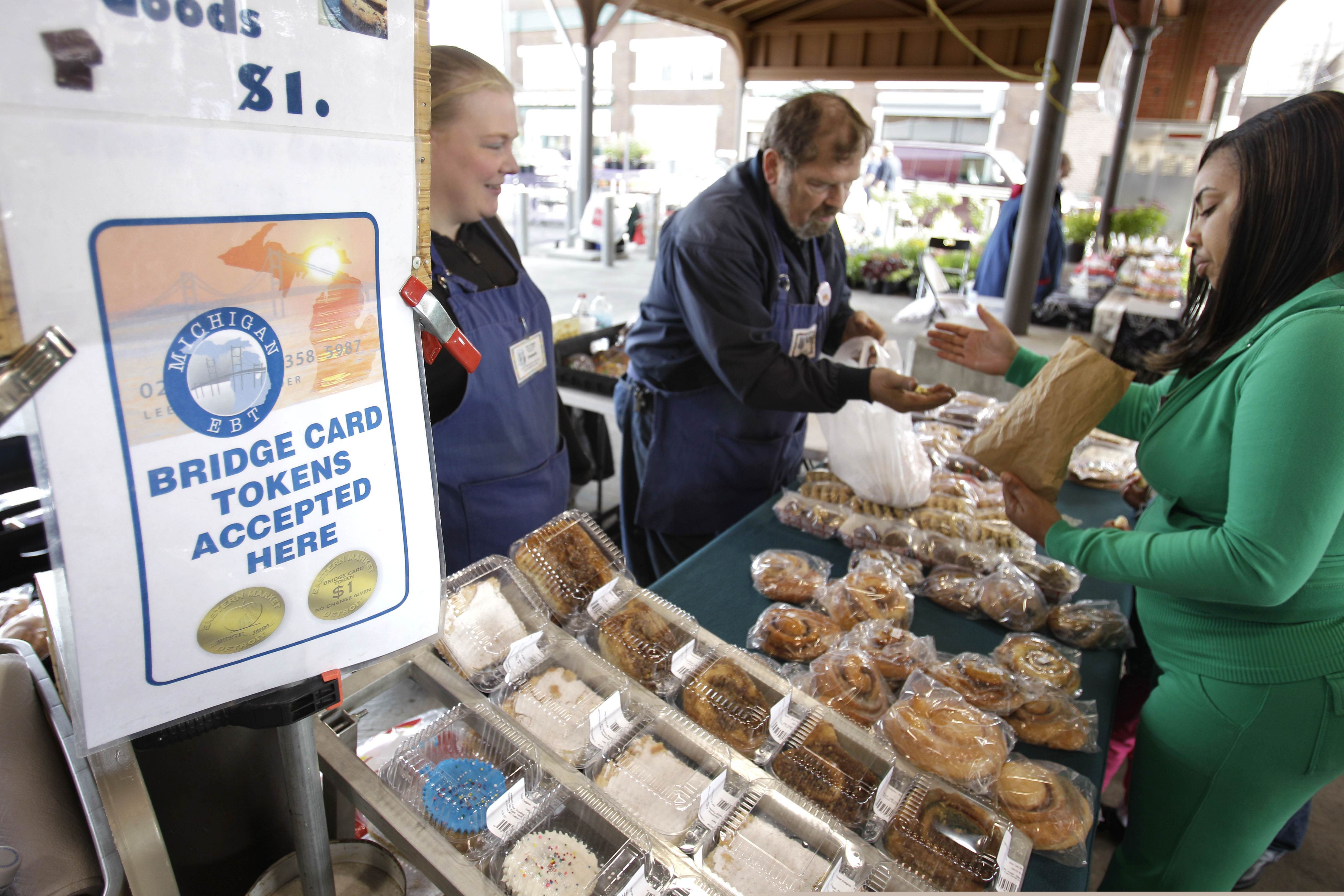 Temeka Williams, right, of Detroit, uses her bridge card tokens for a purchase from Elizabeth and Gary Lauber from Sweet Delights at the Farmer's Market in Detroit. Farmers, growers and operators of open-air markets are heading into a busy time of the year, in early May 2020, as many states still are under stay-at-home orders for residents and non-essential businesses to slow the spread of the new coronavirus.