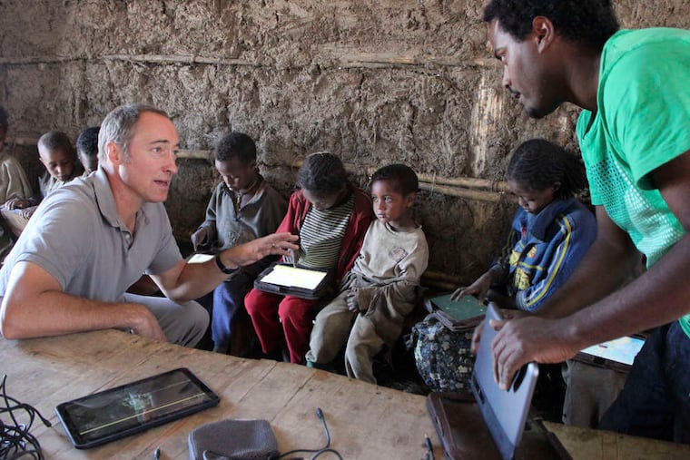 As children in the village of Wenchi use their computer tablets, Matt Keller (left) who is in charge of the One LaptopPer Child project in Ethiopia, speaks with program technician Michael Girma.