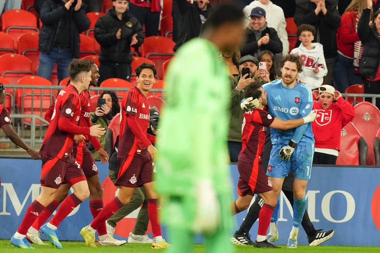 A dejected Andre Blake looks on as Toronto FC goalkeeper Luka Gavran (right) celebrates with teammates after scoring his team's late game-tying goal on Wednesday night.