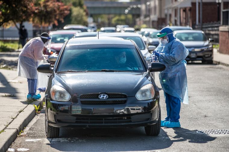 Natasha Thornton, right, and Khadijah Moore, left, work together to administer coronavirus tests to the subjects in the long line of cars, many that had waited for over two hours, at the Stephen and Sandra Sheller Family Health Service Center in Philadelphia.